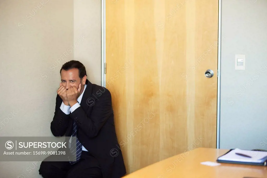 Businessman crouching in corner with terrified expression