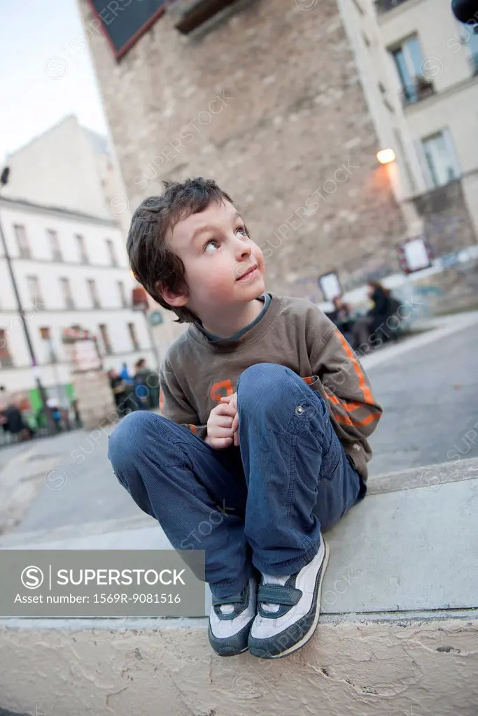 Boy sitting on curb, looking up