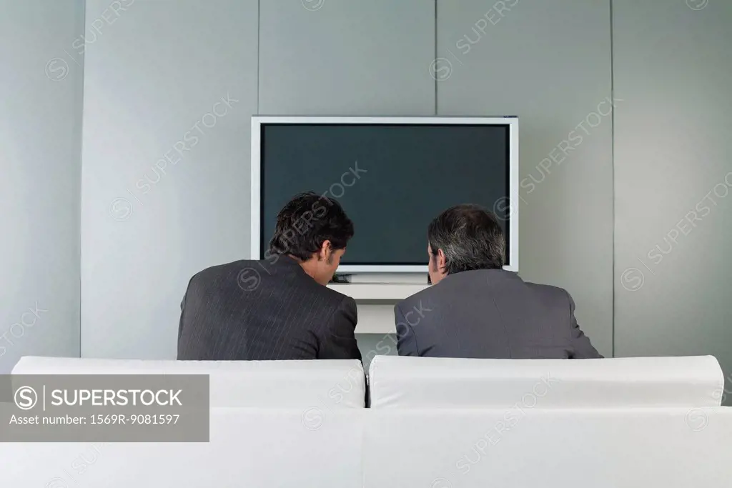 Businessmen sitting on couch in front of television