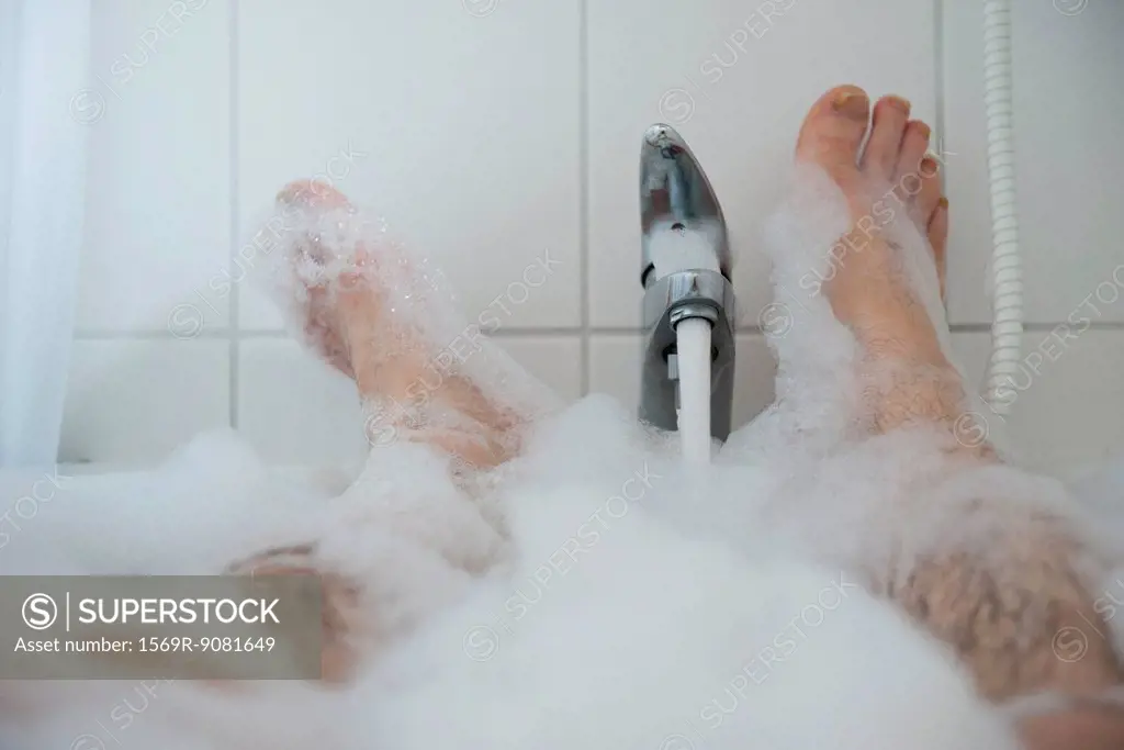 Man soaking in bubble bath, low section