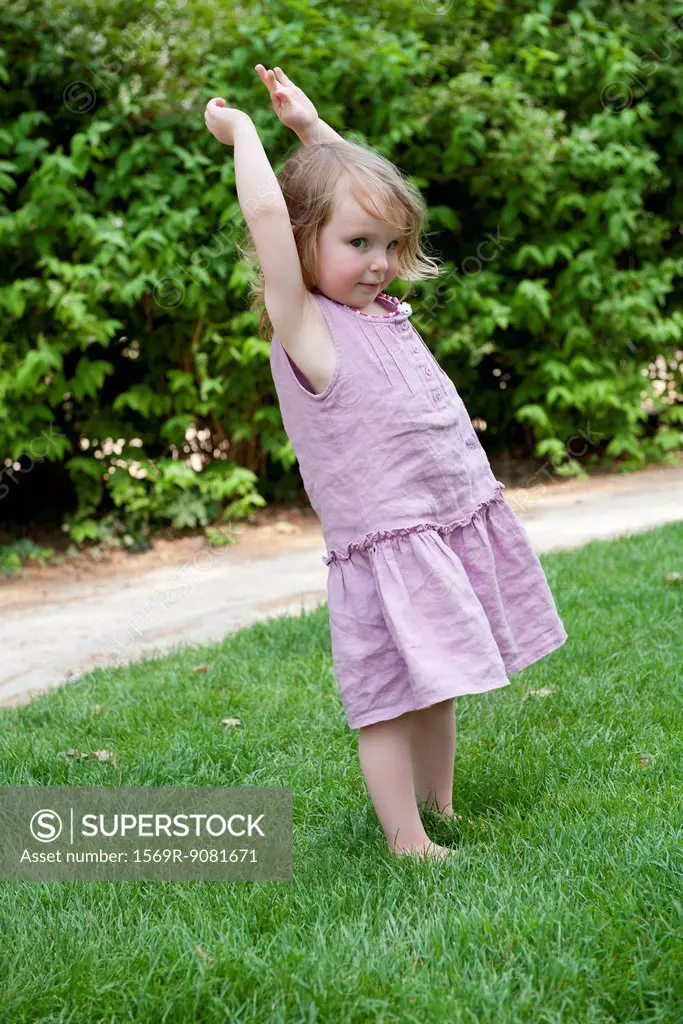 Little girl standing outdoors with arms raised