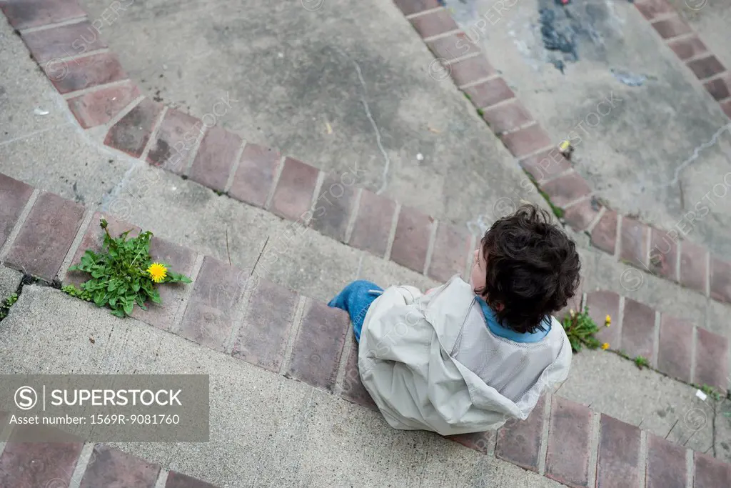 Boy sitting alone on steps, looking away in thought