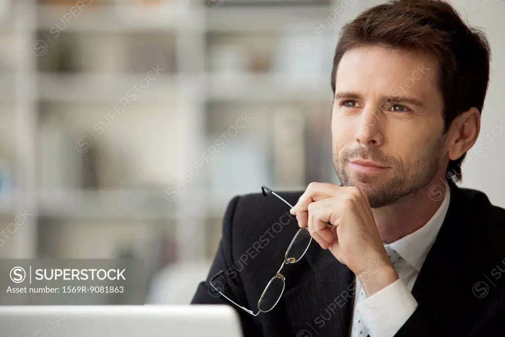 Businessman looking away in thought, glasses in hand