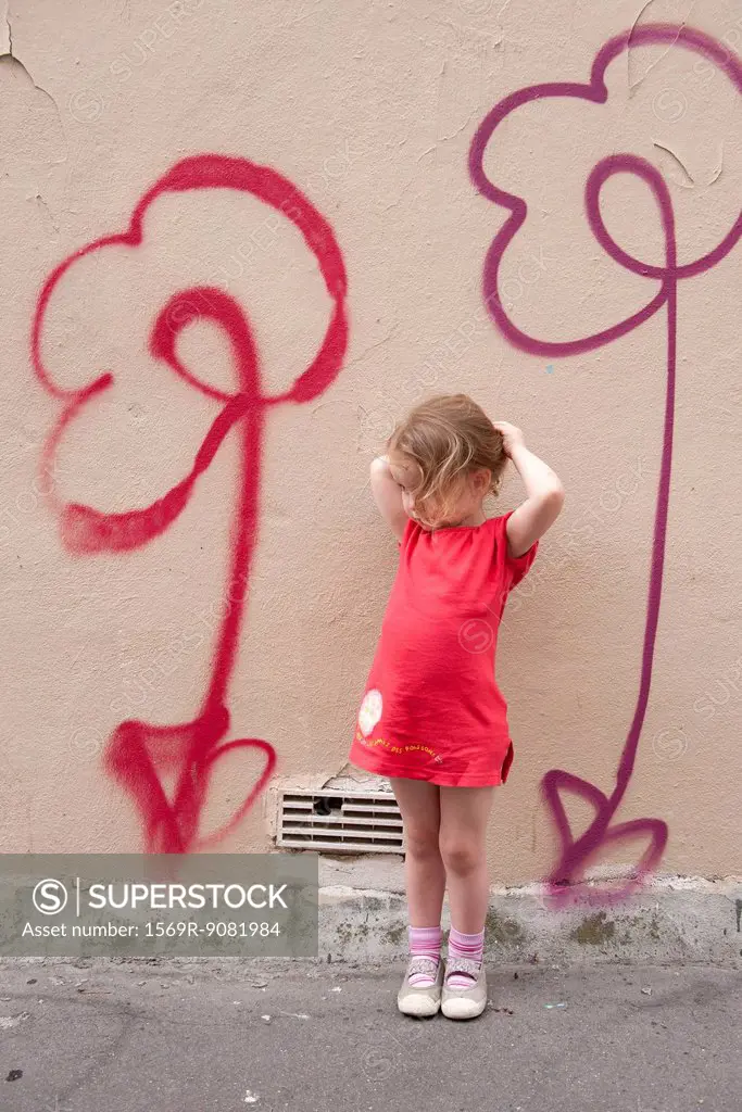 Little girl leaning against wall with flower graffiti, portrait