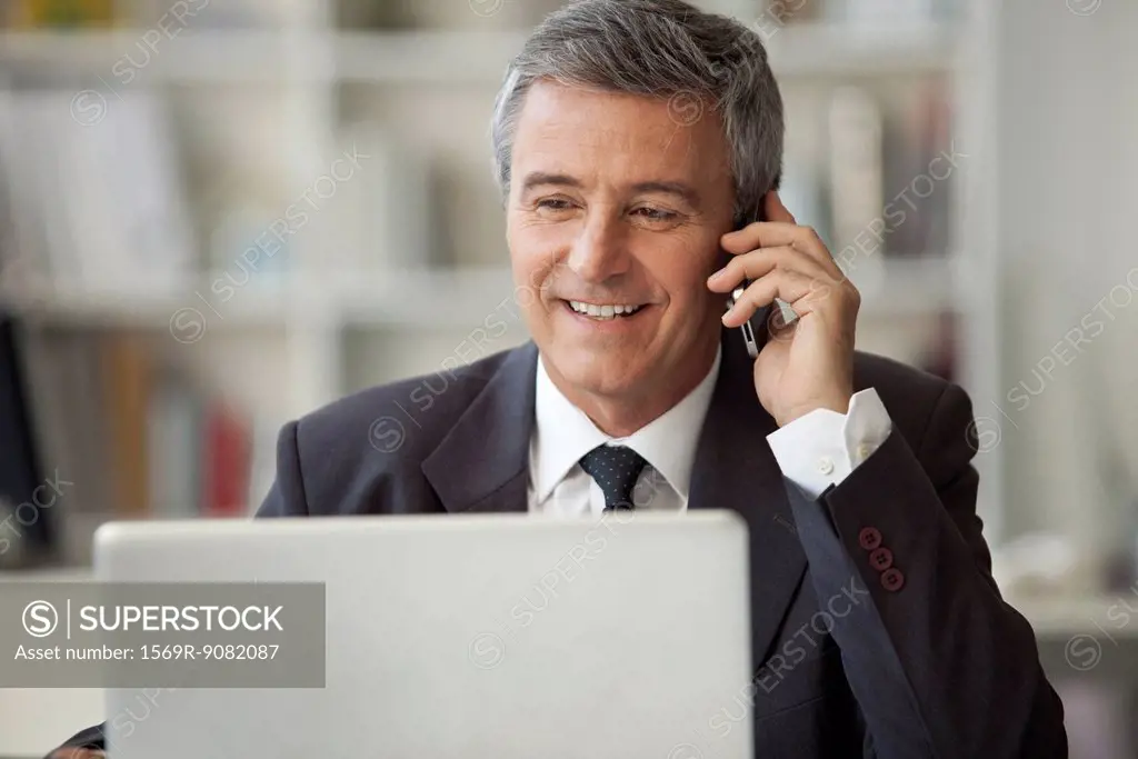 Mature businessman talking on cell phone and using laptop computer