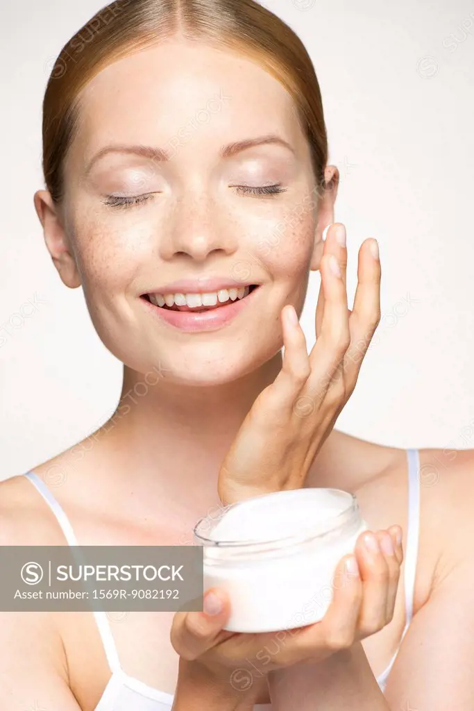 Youn woman moisturizing face with eyes closed