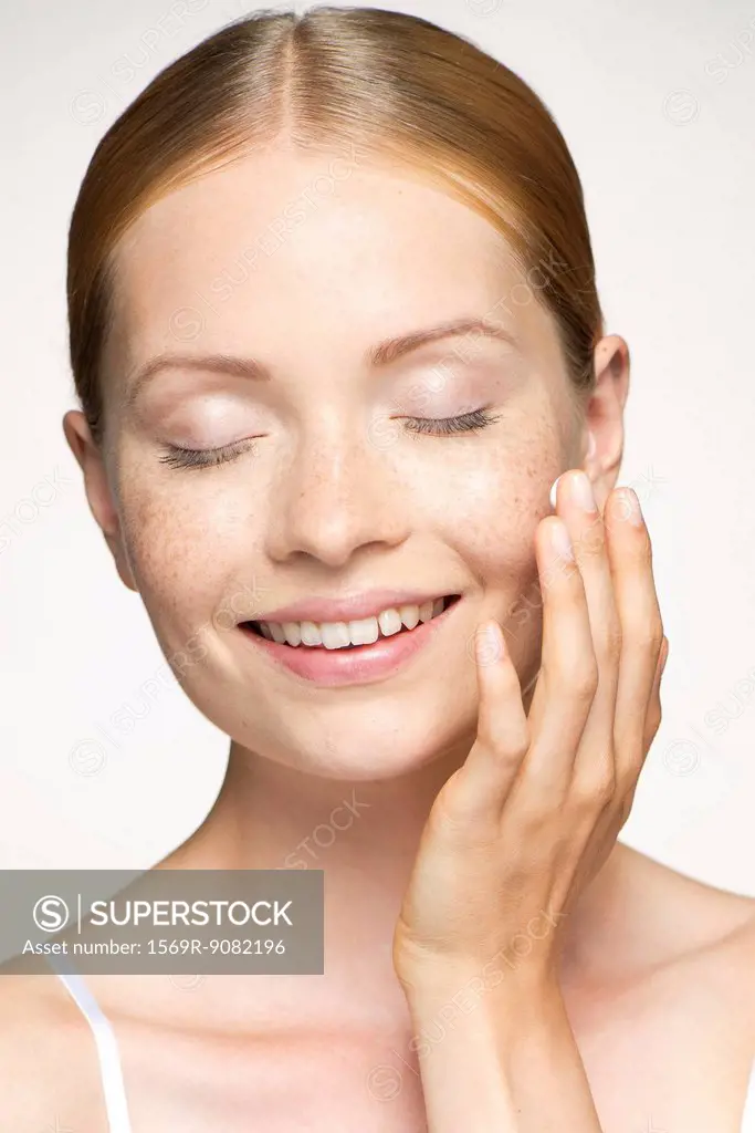 Young woman moisturizing face, eyes closed