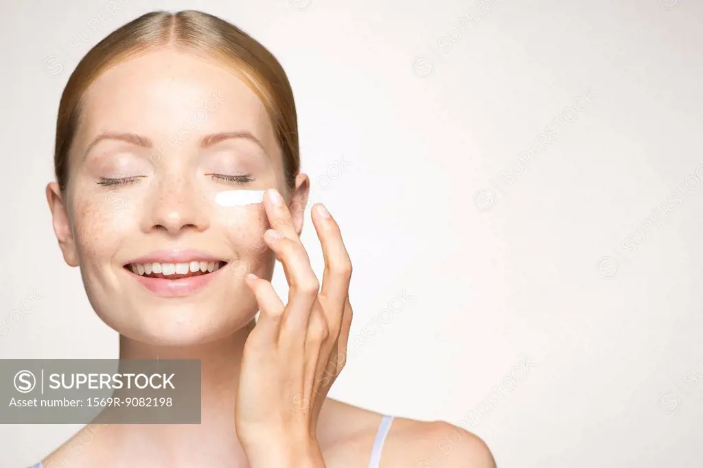 Young woman applying mositurizer under eye