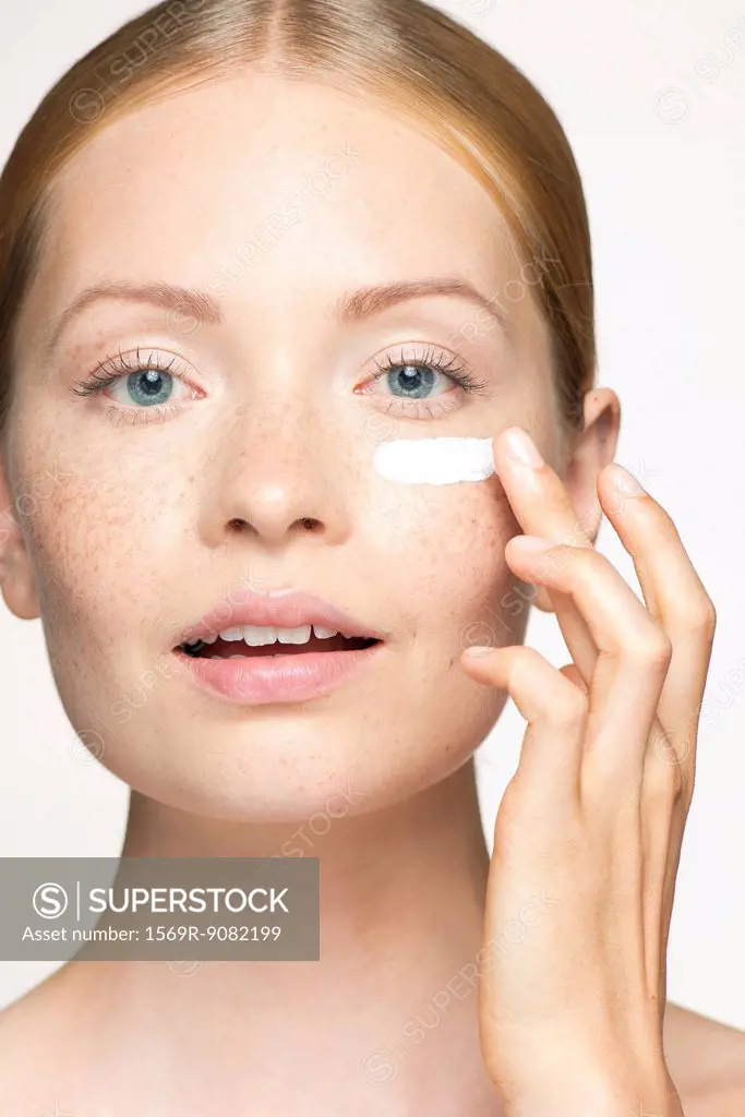 Young woman applying moisturizer under eye