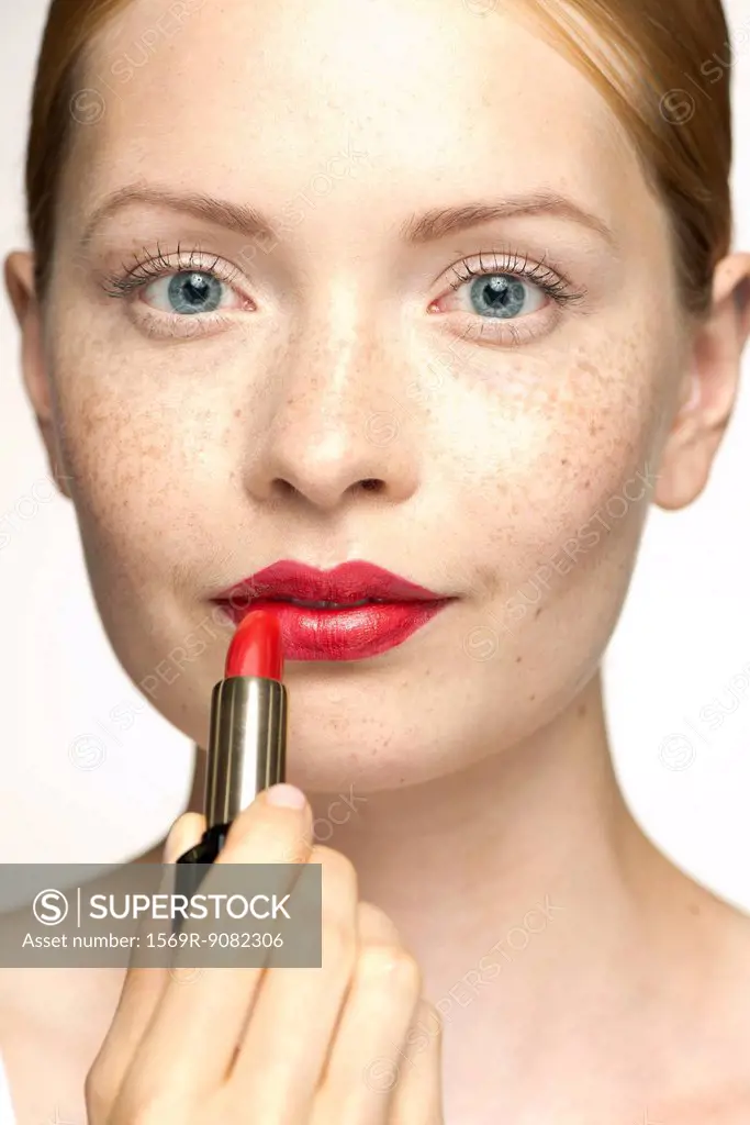 Young woman applying lipstick, portrait