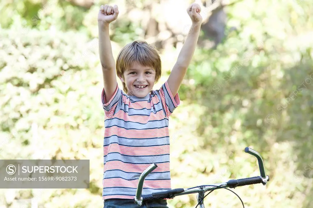 Boy riding bicycle, arms raised, portrait