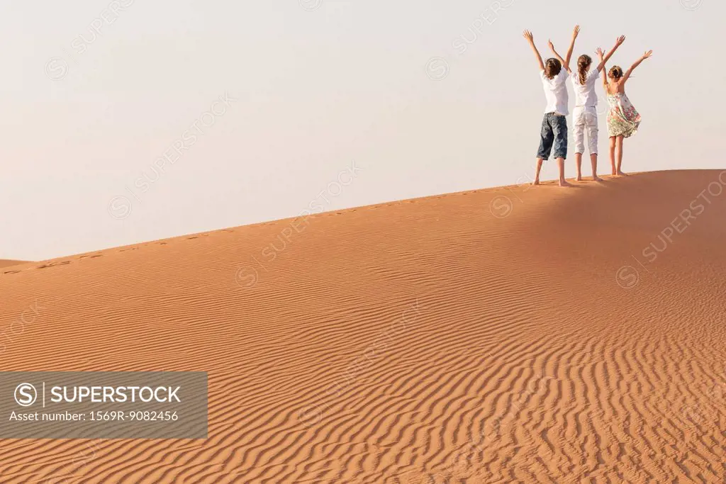 Children standing in desert with arms raised in air