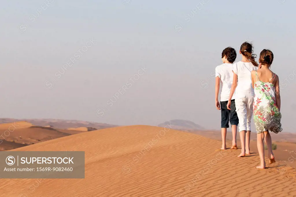 Children walking in desert, rear view