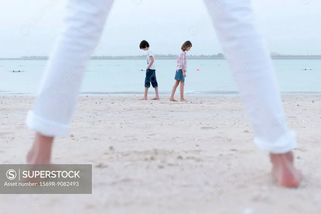 Girl standing on beach, watching siblings at water's edge