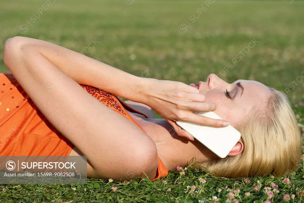 Young woman lying on grass talking on smartphone