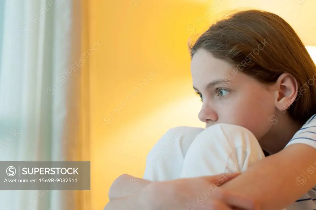 Preteen girl hugging knees, looking away in thought