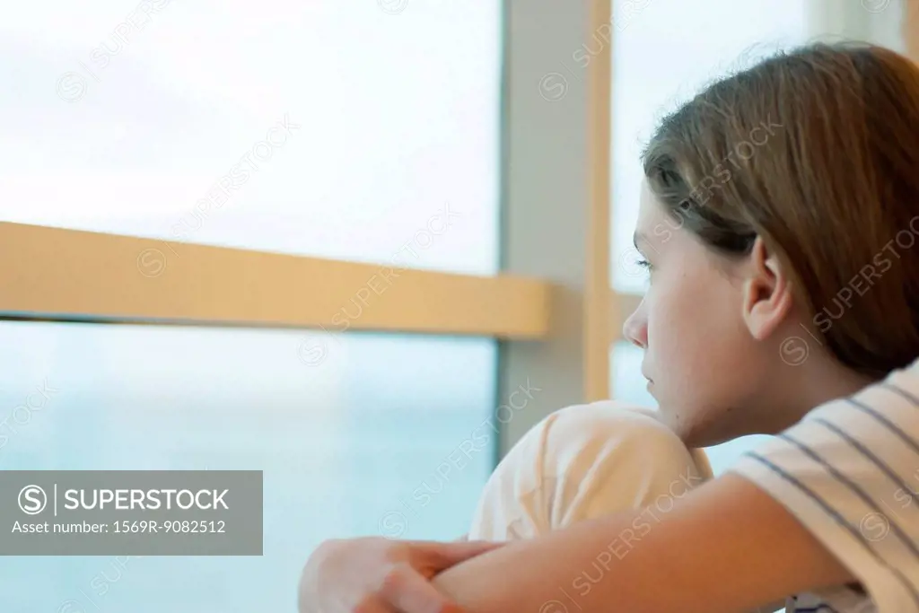Preteen girl hugging knees, looking out window