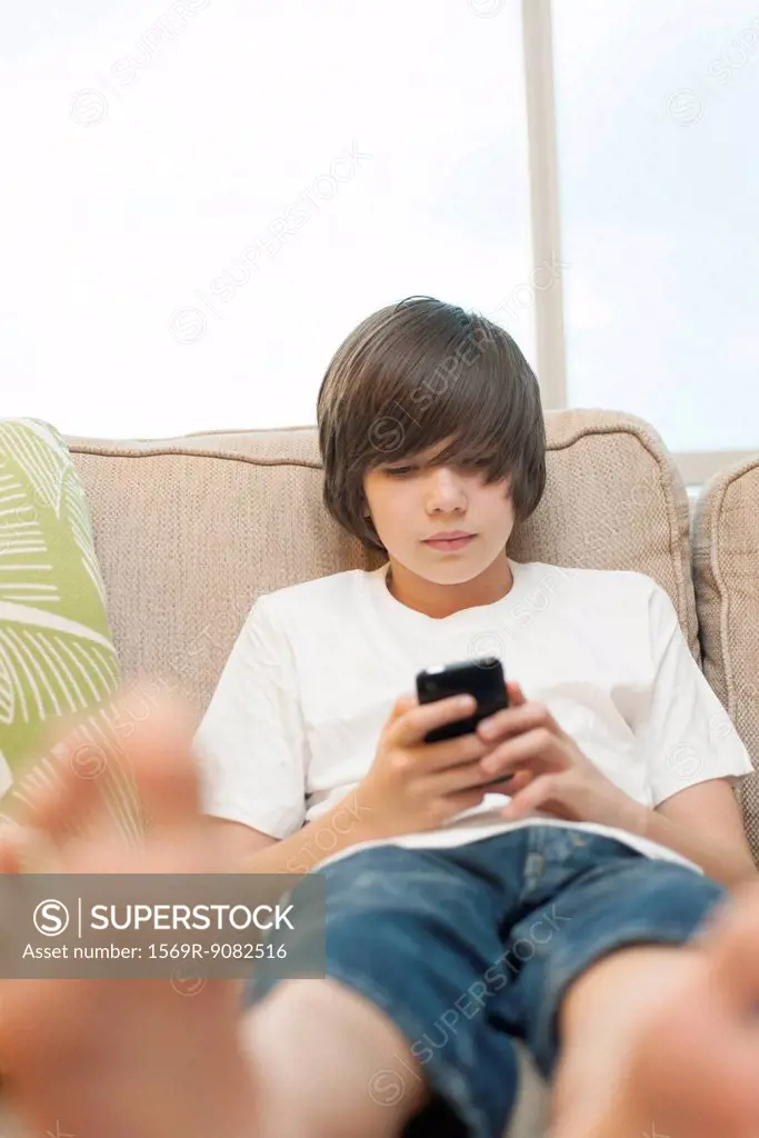 Teenage boy sitting on sofa, using smartphone