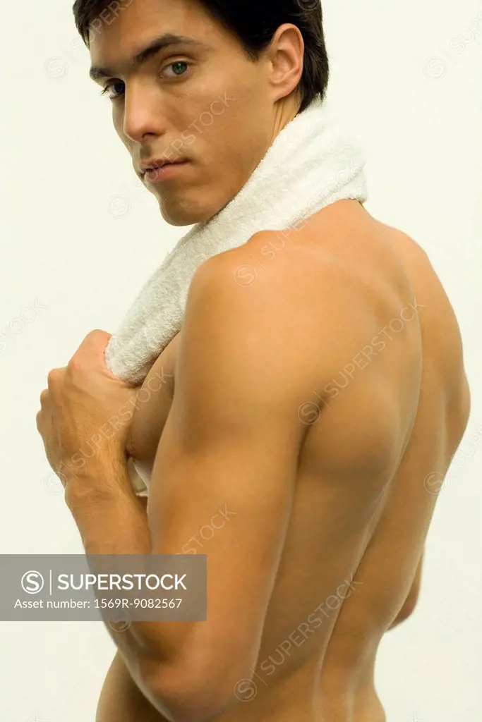 Barechested man with towel around neck, looking over shoulder at camera