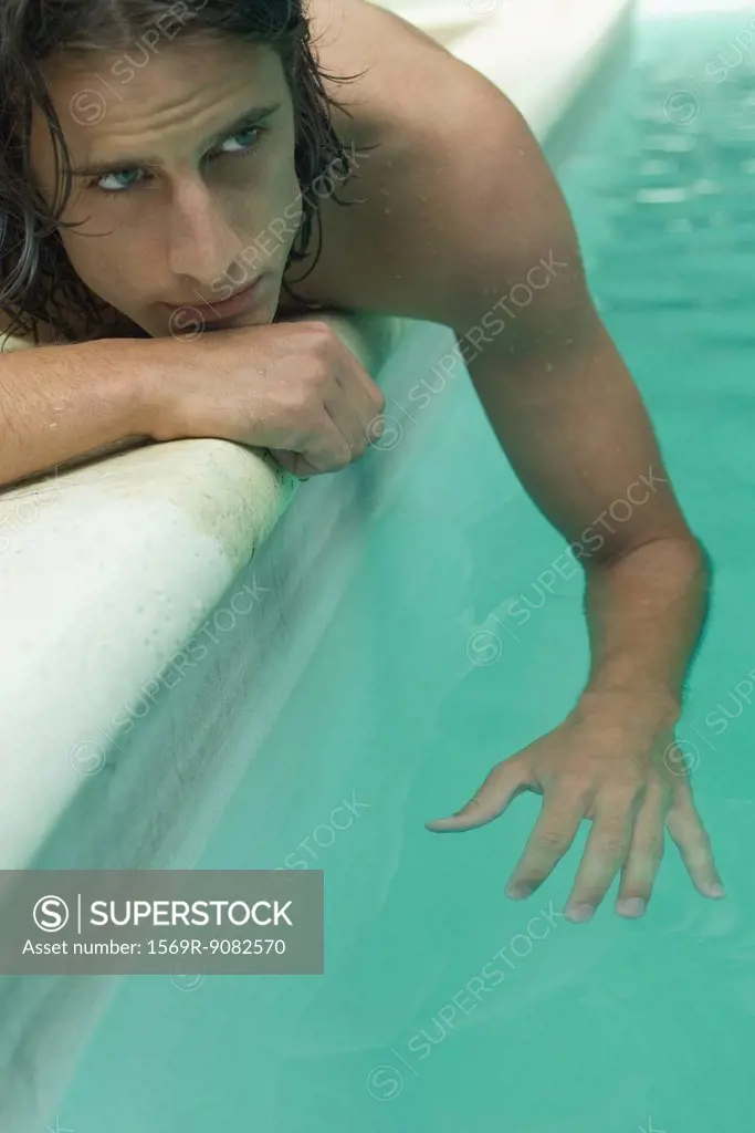 Young man lying beside swimming pool, dangling arm in water