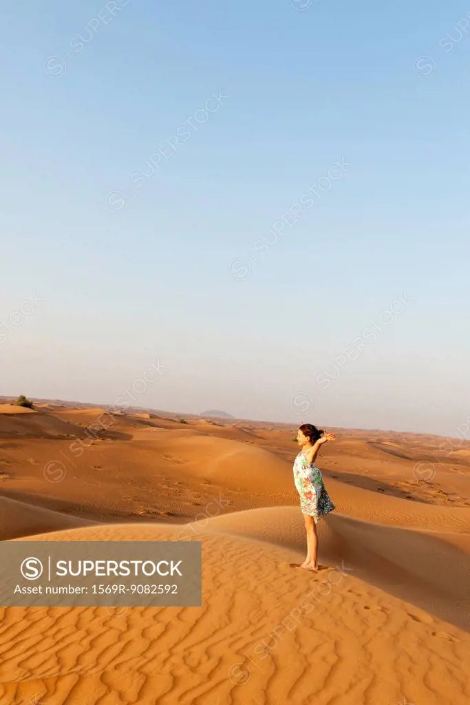 Girl standing in desert with arms raised in air