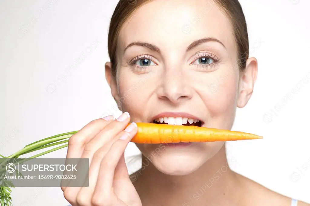Young woman biting into carrot, portrait