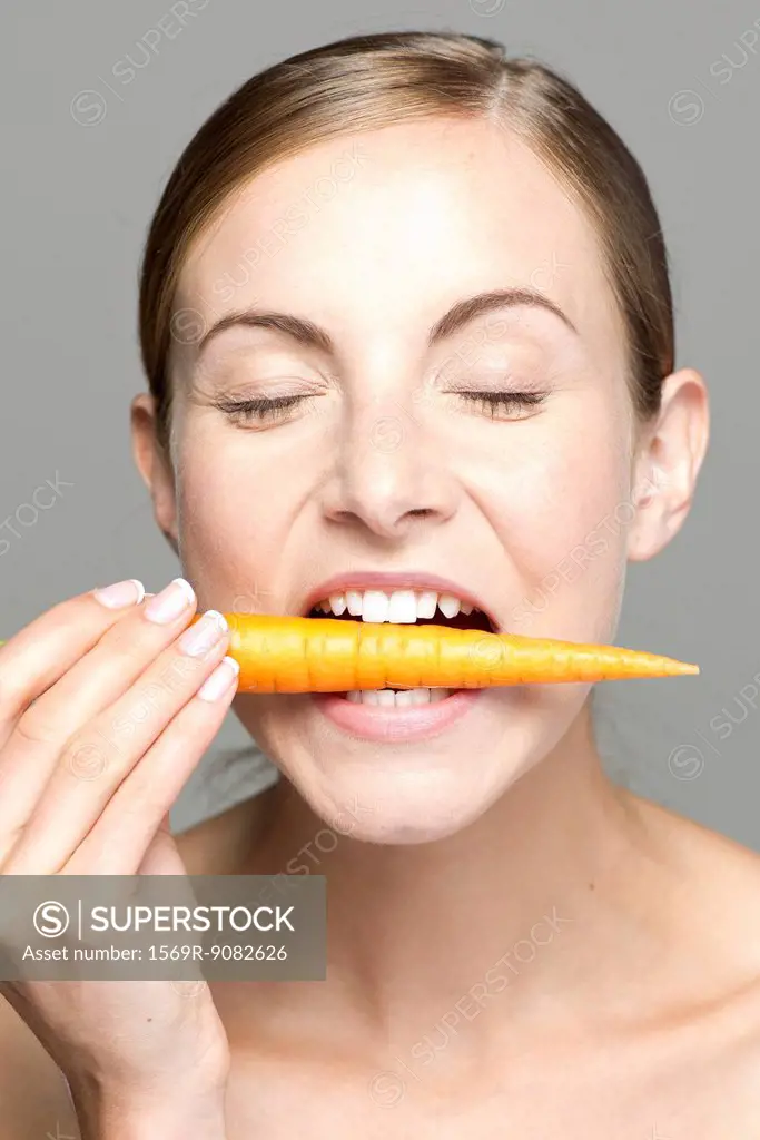 Young woman biting into carrot, eyes closed