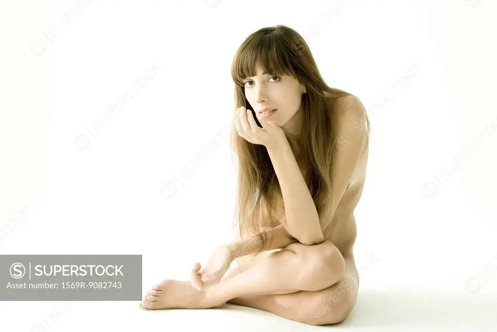 Nude woman sitting with arms crossed over chest, hand under chin