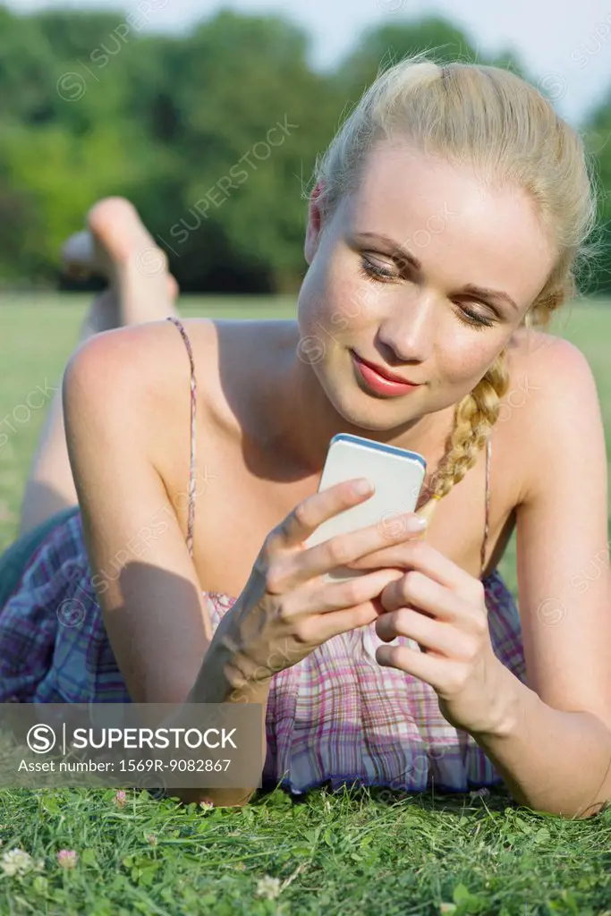 Woman lying on grass, using smartphone