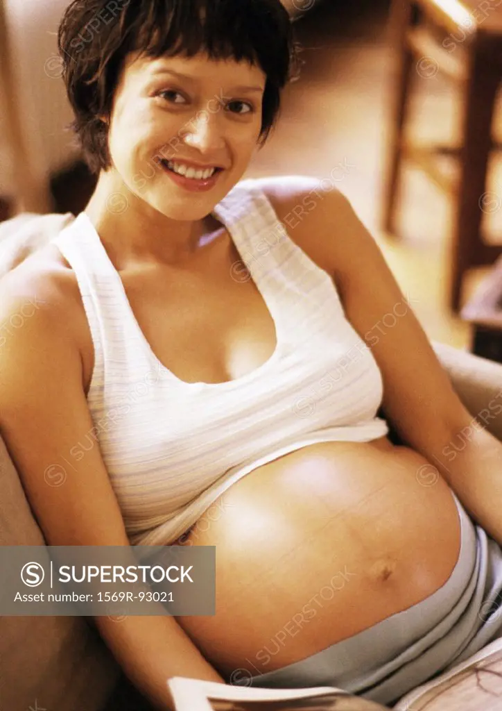 Pregnant woman sitting in armchair, smiling at camera, portrait