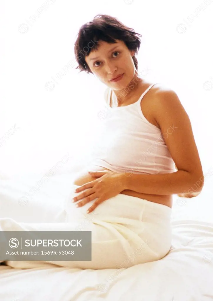 Pregnant woman sitting with hand on stomach, looking at camera, portrait