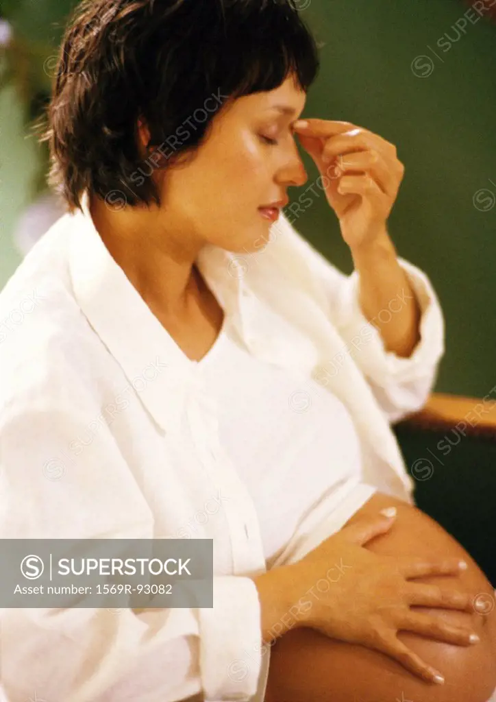 Pregnant woman with hand on stomach, touching bridge of nose