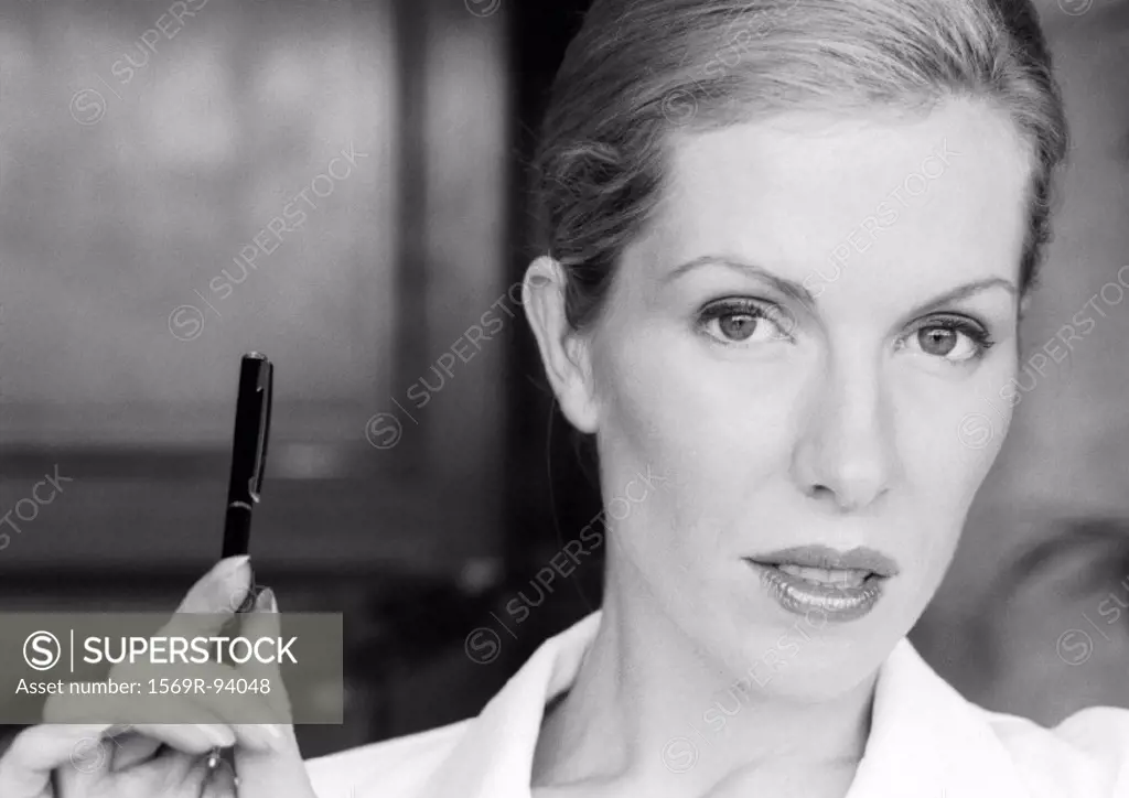 Businesswoman holding up pen, close-up portrait, B&W