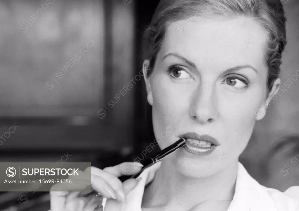 Businesswoman holding pen at corner of mouth, close-up, B&W