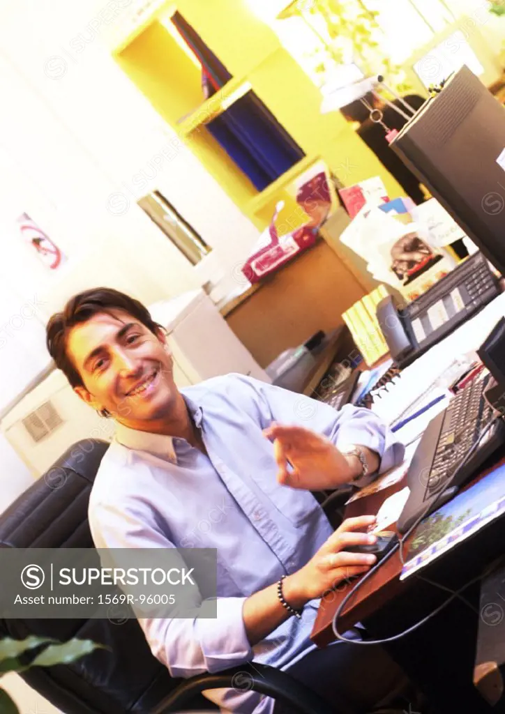 Man working at desk in office, smiling at camera