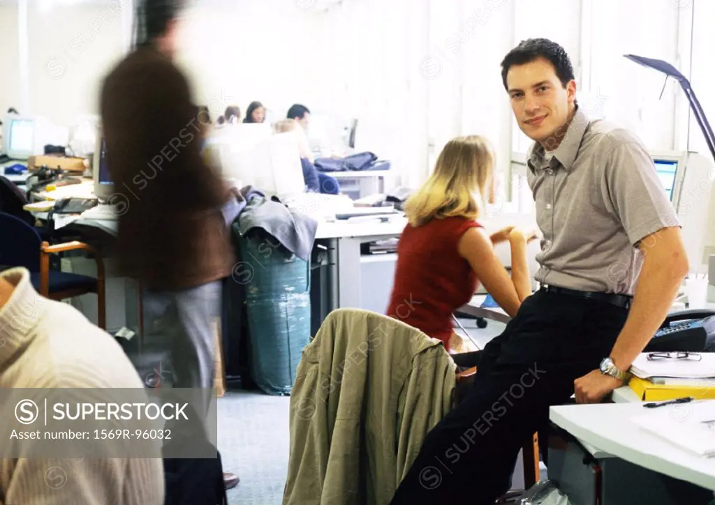 Man sitting on desk in office, looking at camera