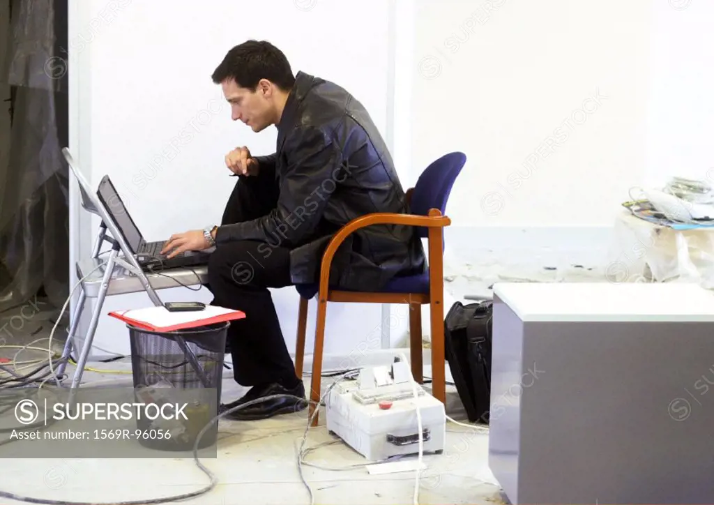 Man working on laptop on chair, side view