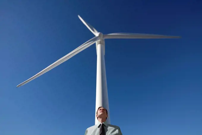 Businessman leaning against wind turbine