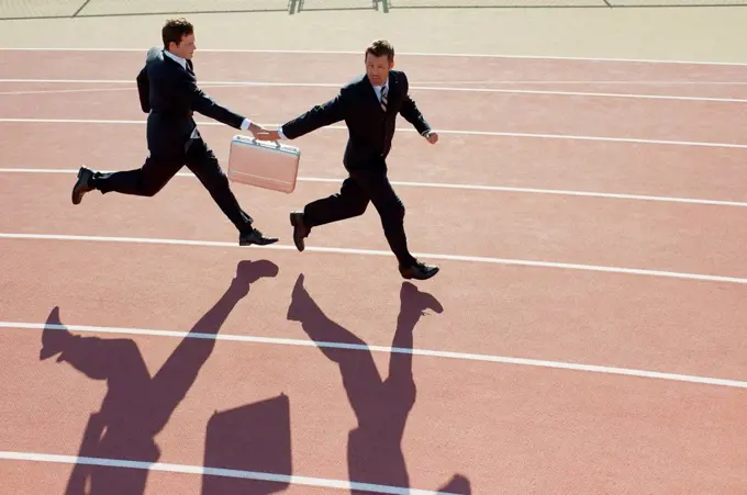 Businessmen passing briefcase while running on running track