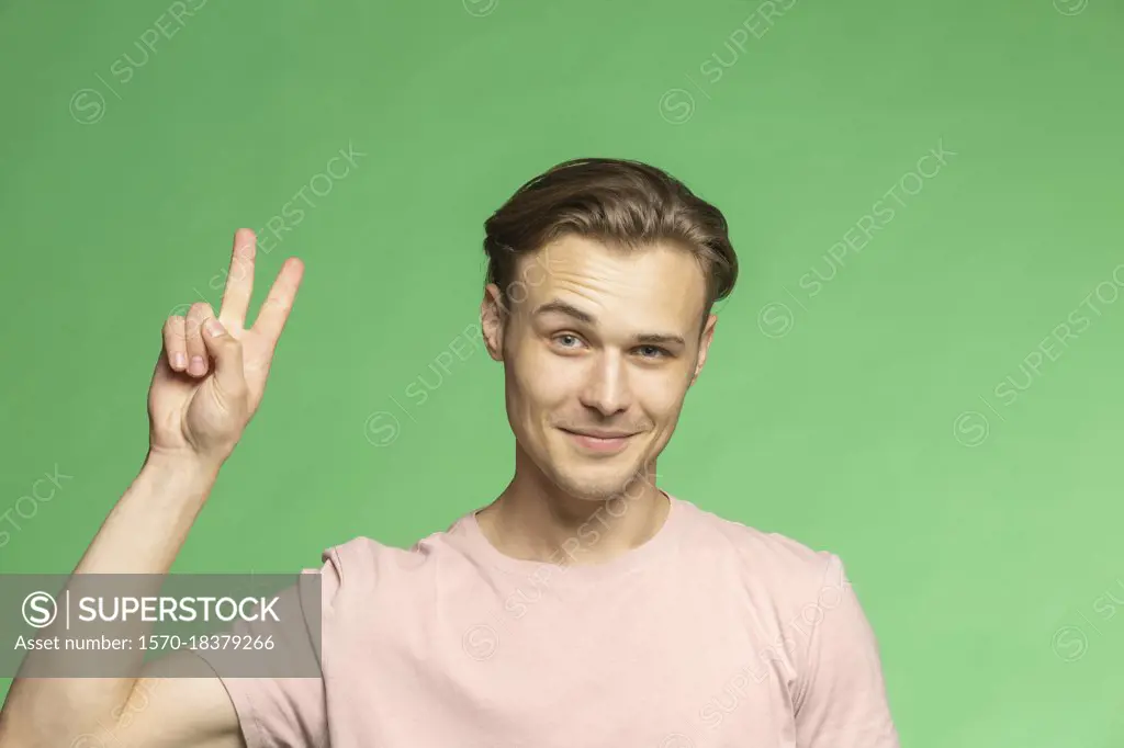 Portrait confident young man gesturing peace sign on green background
