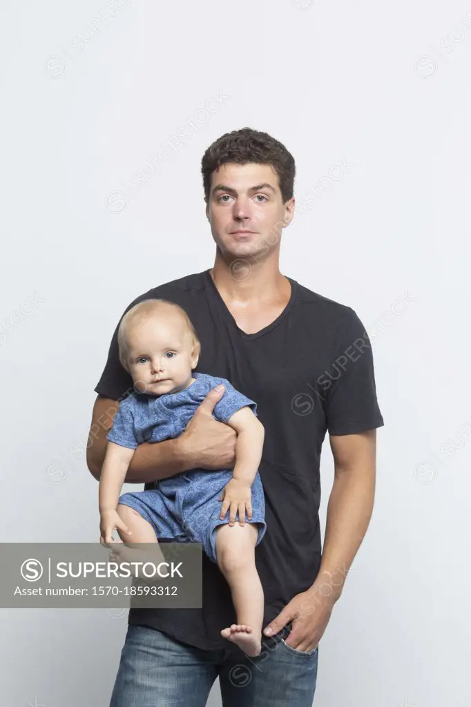 Portrait confident father holding baby son on white background
