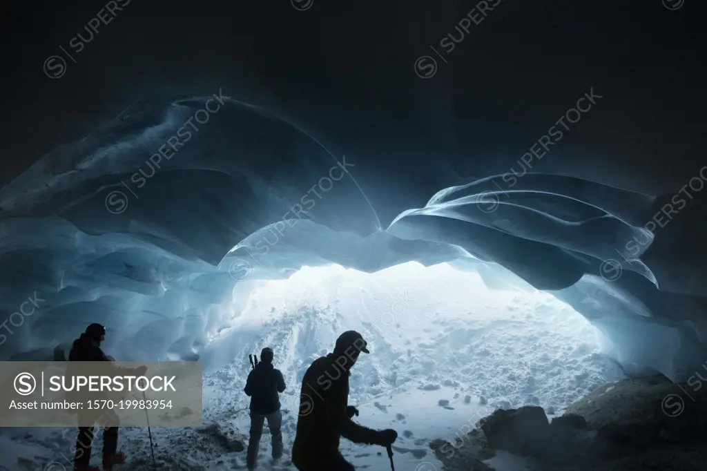 Silhouetted men hiking in glacier ice cave, Selkirk Mountains, Canada