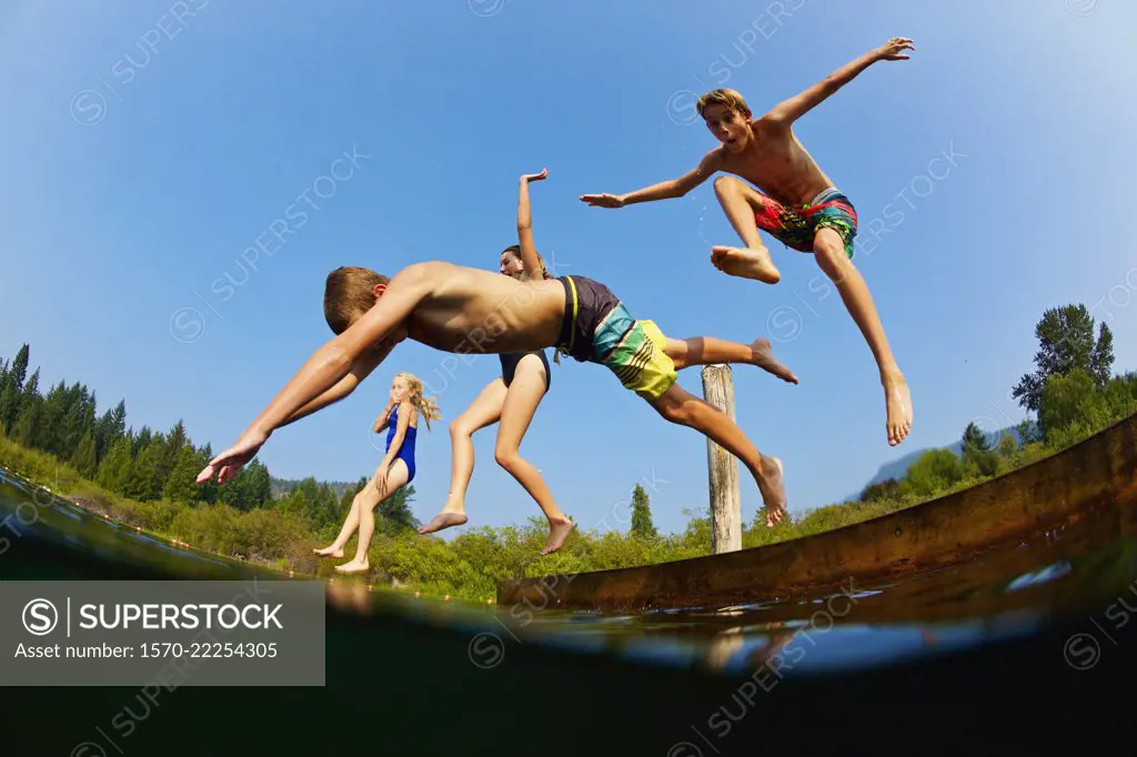 Playful kids jumping off dock into sunny summer lake