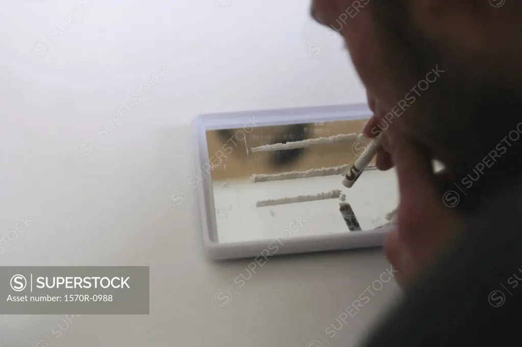 Man holding rolled bank note over lines of cocaine
