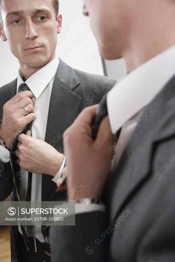 A man straightens his tie in a mirror