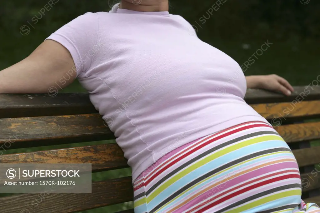 Midsection of a pregnant woman sitting on a park bench