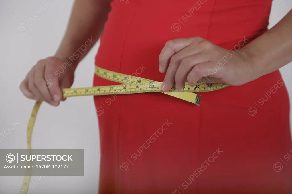 Midsection of a pregnant woman measuring her waist with a measuring tape