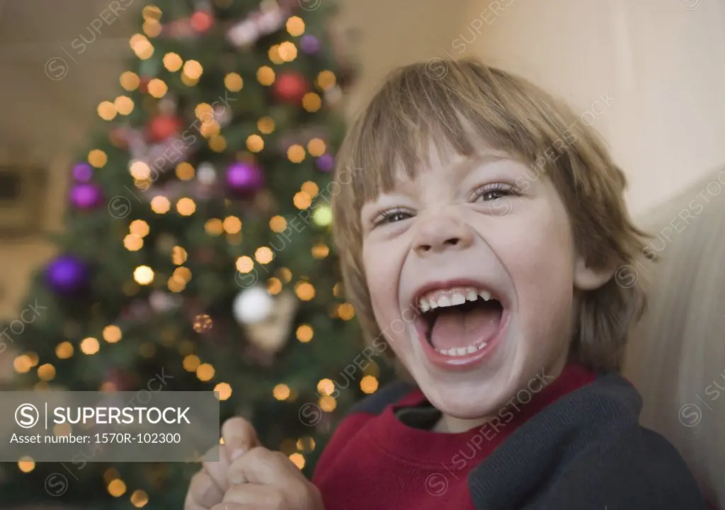 A young boy laughing in front of a Christmas tree