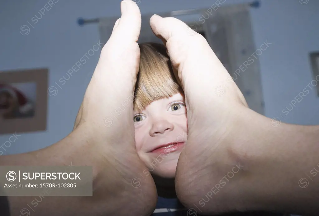 A young boy's smiling face between a person's feet