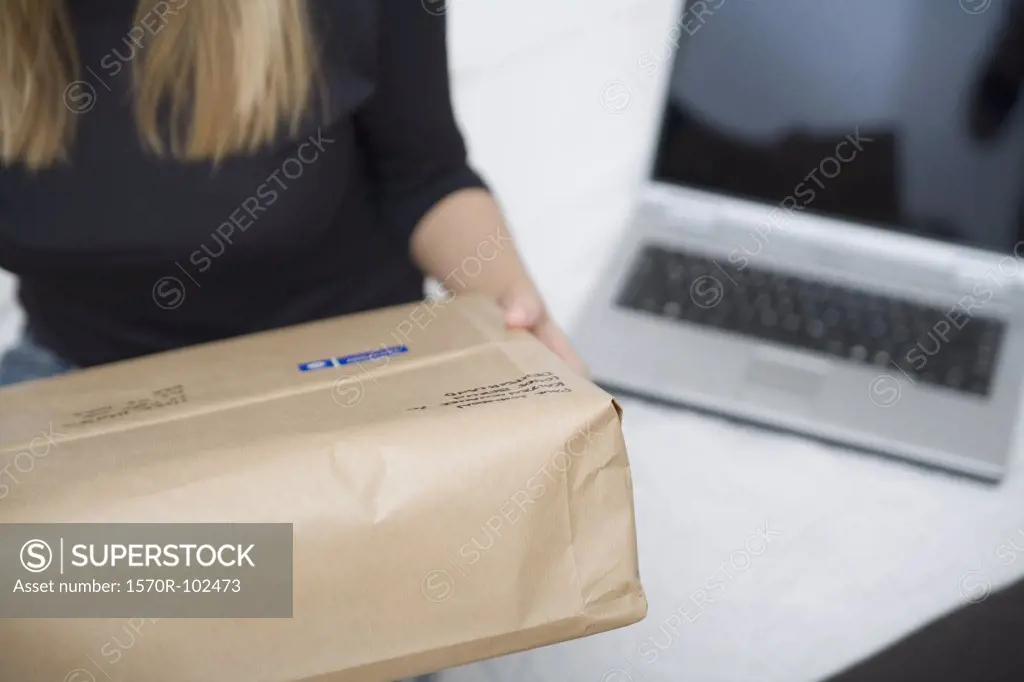 Young woman sitting on a bed holding a parcel next to her laptop